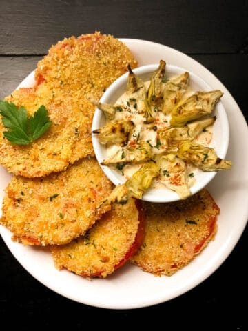 A round white plate filled with Gluten Free Fried Creole Tomatoes with Roasted Artichoke Remoulade against a black background.