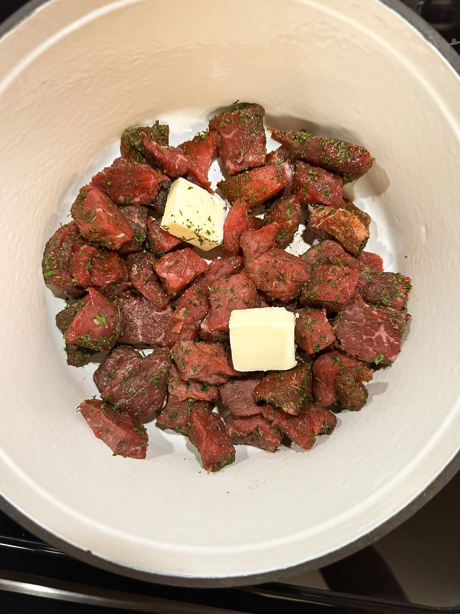 Seasoned round steak pieces with butter in a red enameled cast iron Dutch oven.