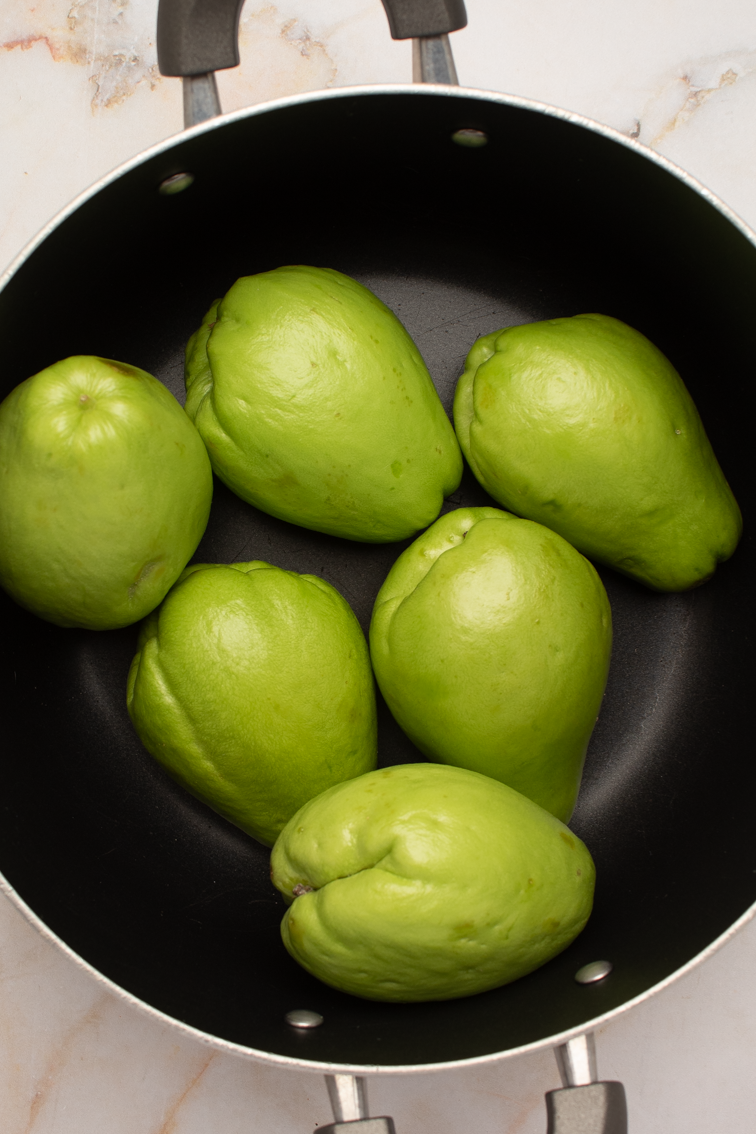Six fresh mirliton (chayote squash) in the bottom of a black pot.
