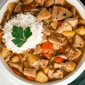 Turkey stew in a round white bowl with rice on top and a whole parsley garnish alongside a green linen napkin.