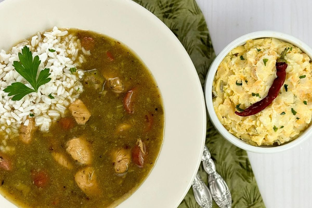 Chicken and sausage gumbo in a round white bowl alongside Cajun potato salad. 