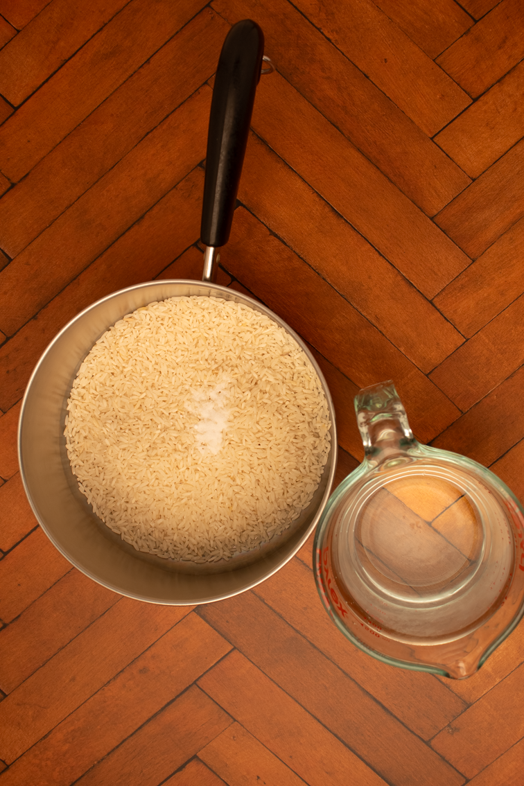 A pot filled with rice and salt alongside and a Pyrex glass jug filled with water.