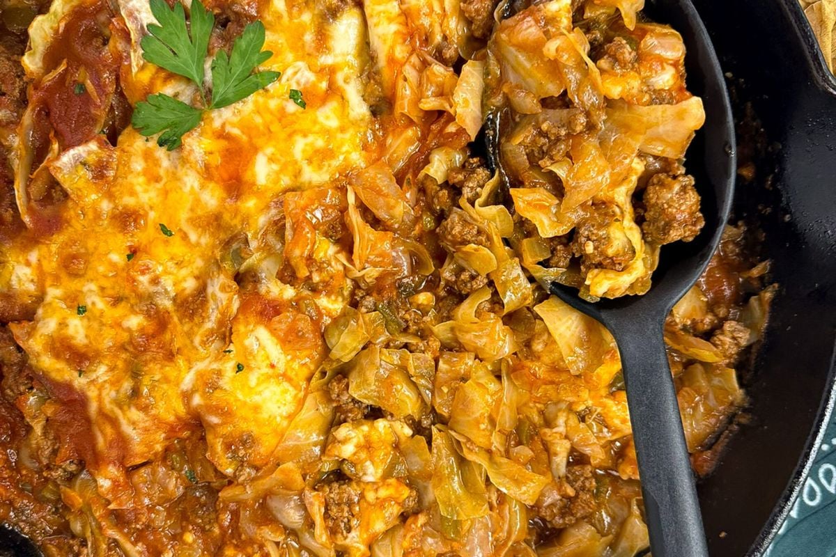 Cajun cabbage casserole with a black serving spoon in a black cast iron skillet. 