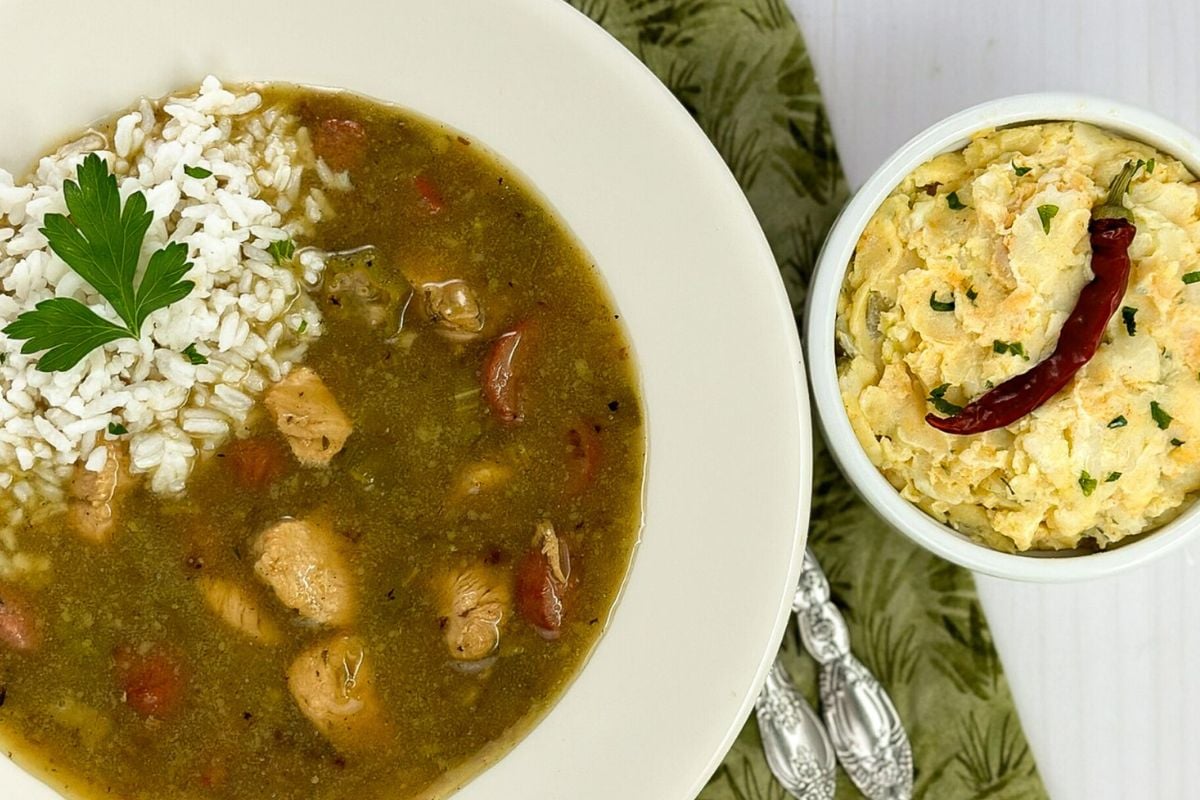 Chicken and sausage gumbo alongside a small white bowl filled with potato salad. 