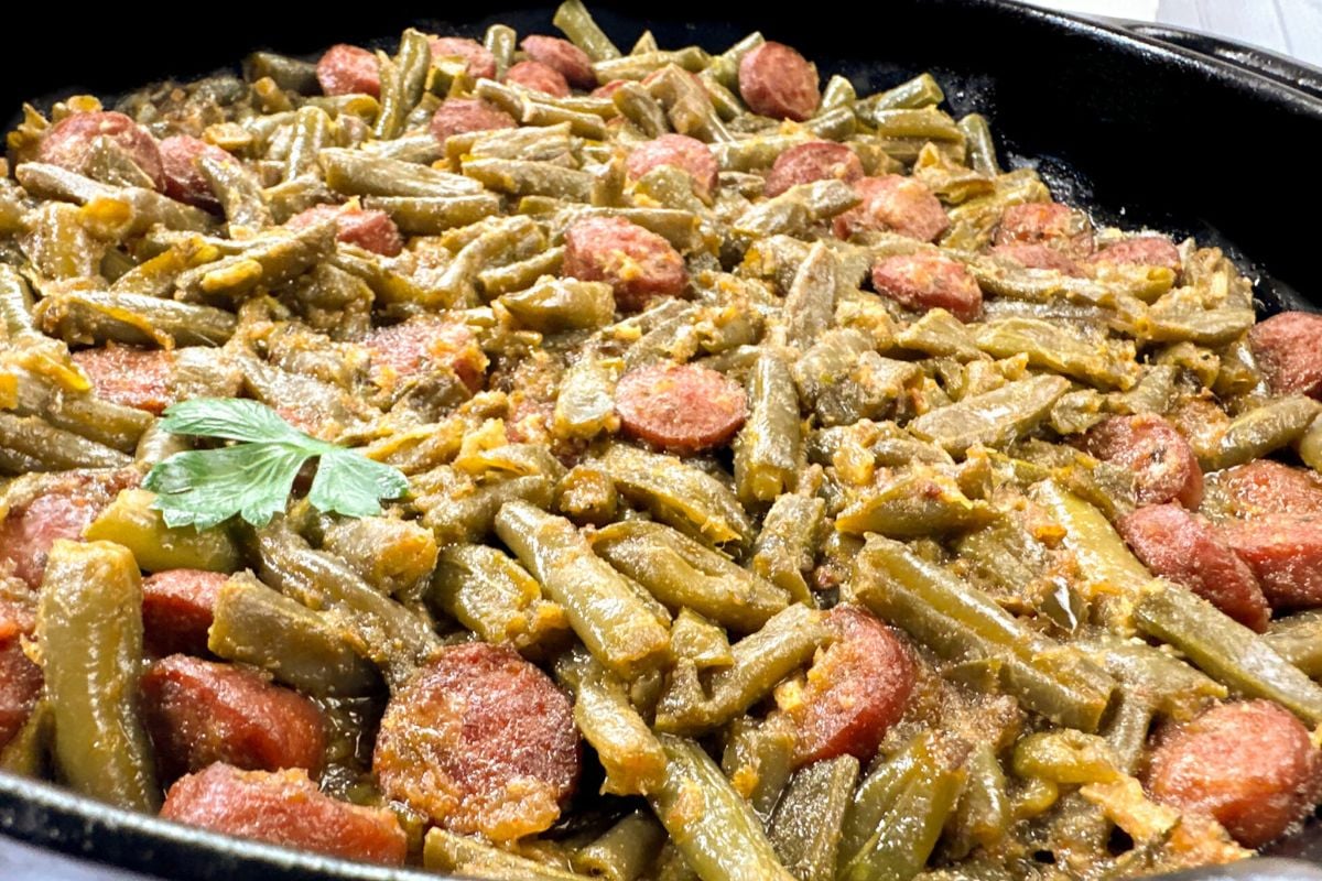 Cajun smothered green beans with sausage in a black cast iron skillet.