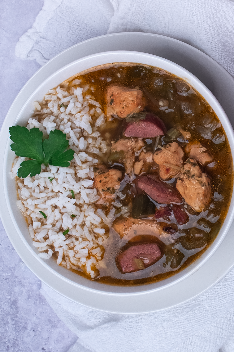 Closeup of chicken and sausage gumbo with rice in a round white bowl.
