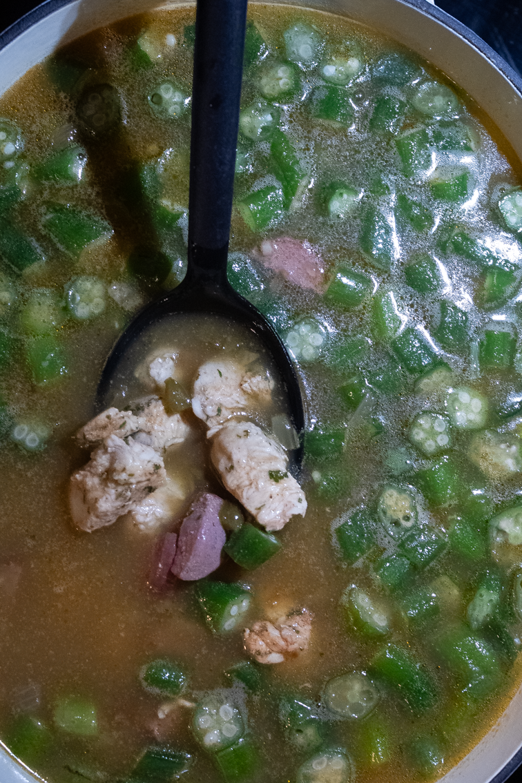 Chicken, sausage, okra, broth and roux for gumbo in a pot.