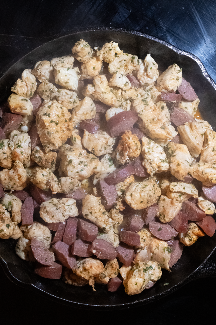 Browned sausage and chicken cubes in a pan.