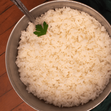 Freshly cooked white rice in a pot alongside a green napkin on a dark wood background.