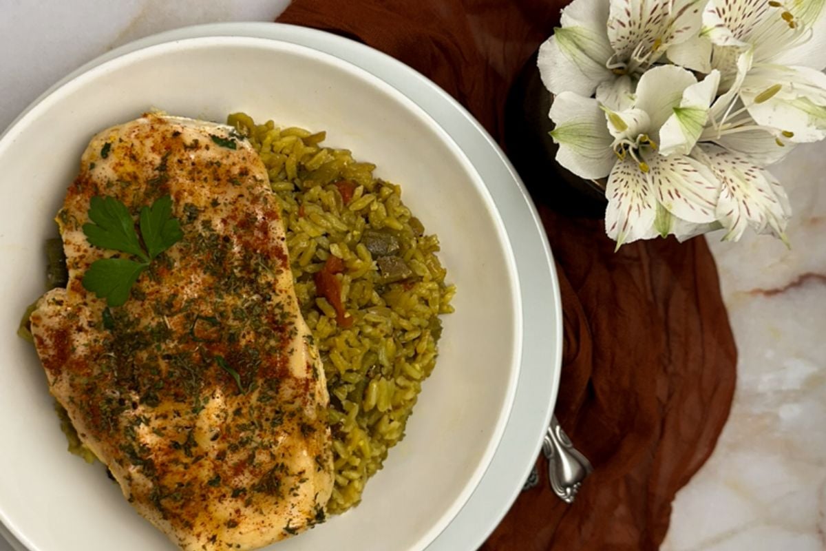 Cajun baked chicken and rice on a round white plate with white flowers and a red napkin. 