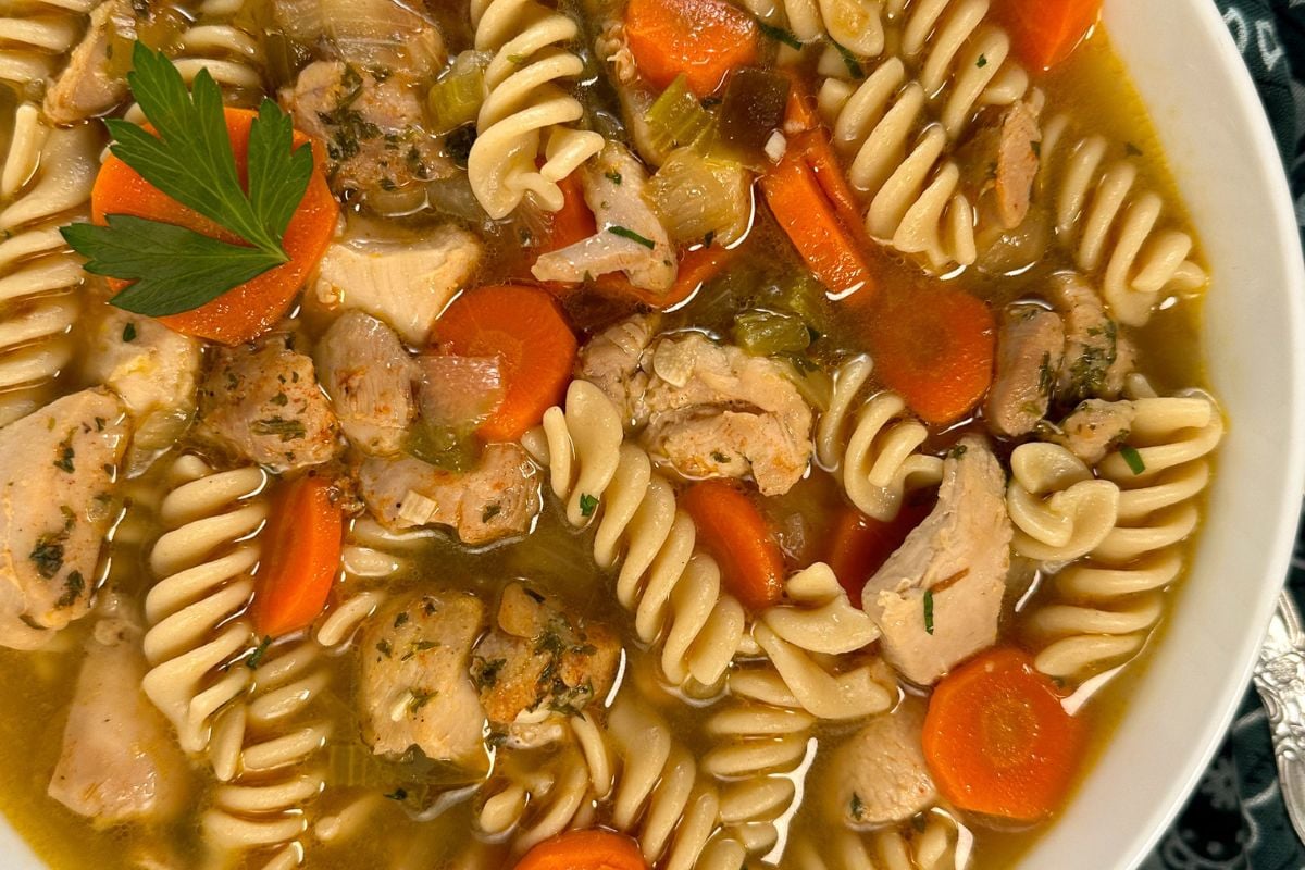 Cajun chicken noodle soup in a round white bowl with a whole parsley leaf garnish in the top left corner. 