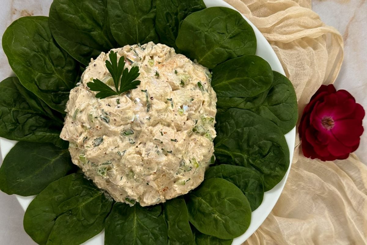 Cajun chicken salad in the middle of spinach leaves atop a round white plate.