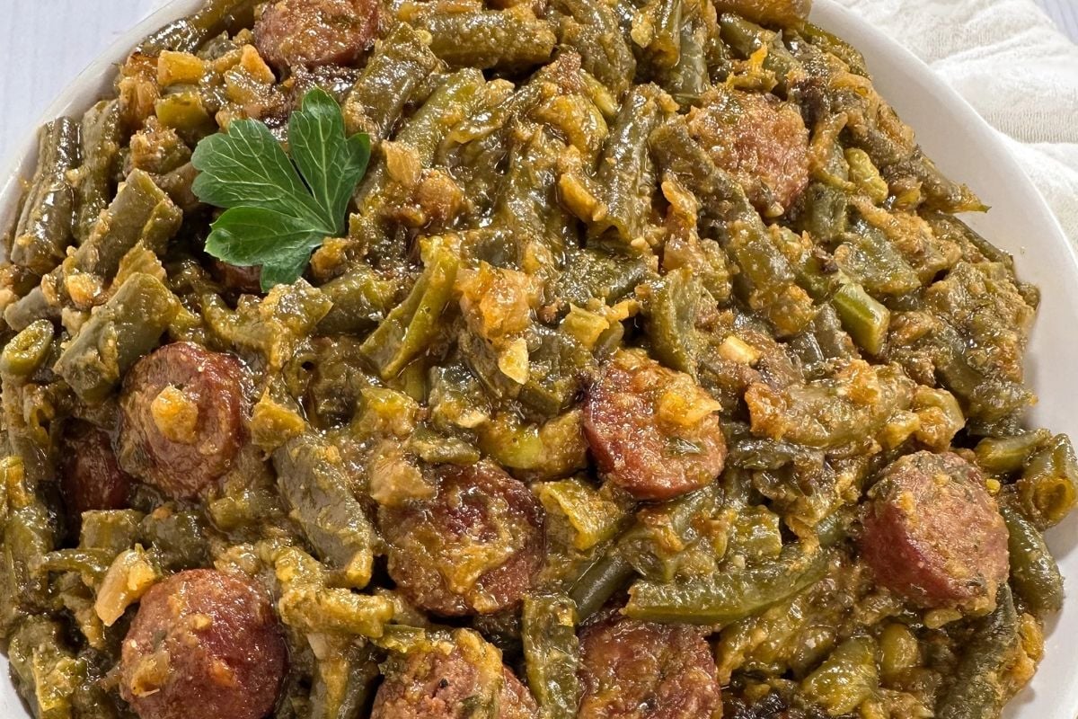 Cajun smothered green beans with sausage in a round white bowl.