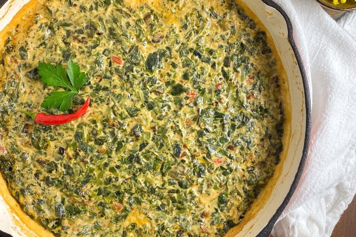 Cajun creamed spinach in a large red enameled cast iron skillet.