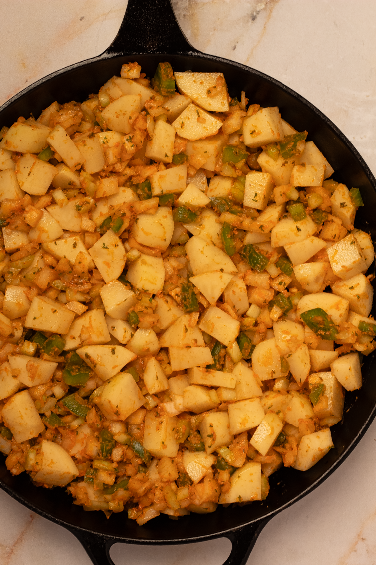 Seasoned potatoes, onions, bell peppers, and celery in a black iron skillet.