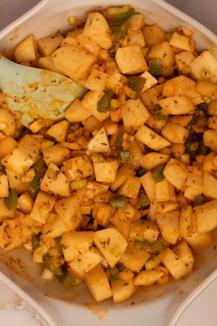 Potato chunks being tossed with freshly chopped veggies and a buttery olive oil sauce with spices.