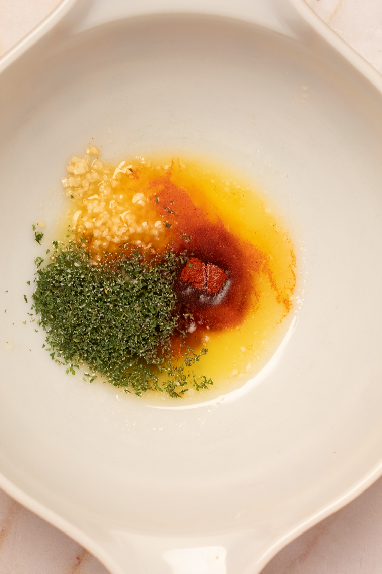 Butter, avocado oil, dried spices, and minced garlic in a large white mixing bowl.