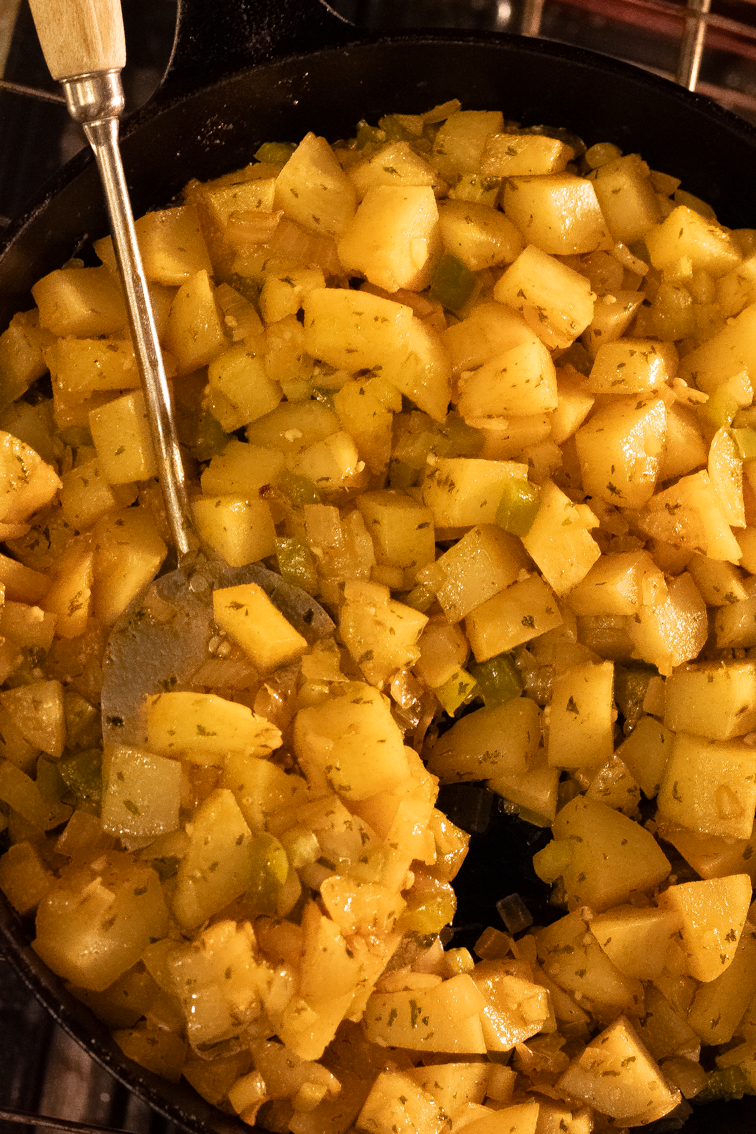 A metal spatula flipping sections of Cajun roasted potatoes over in a large cast iron skillet.