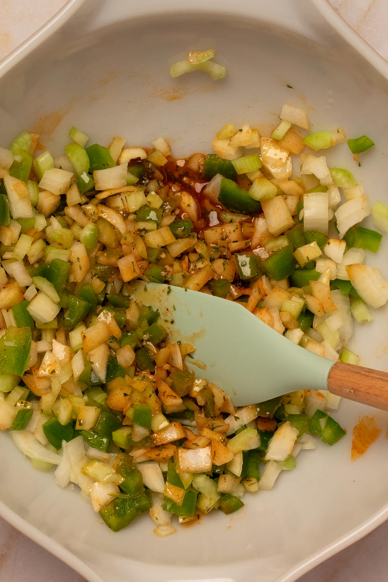 A butter sauce and chopped onion, green bell pepper, and celery in a bowl.
