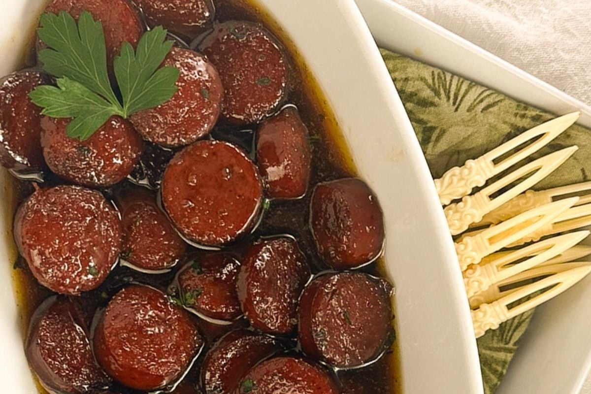 Beef sausage bites in a white serving dish with a green napkin and toothpicks.