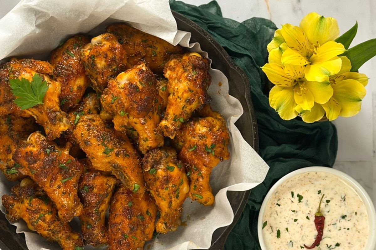 Cajun chicken wings in black cast iron pan alongside Cajun ranch dressing. 