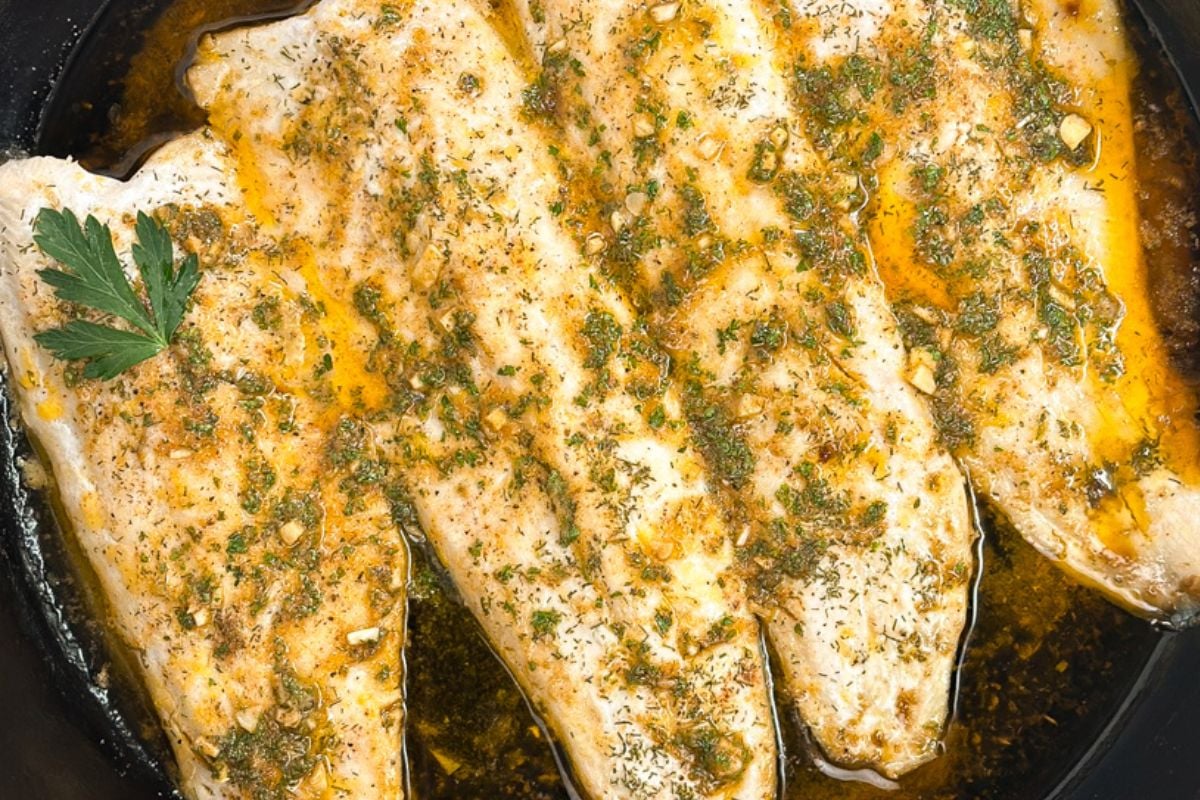 Baked rainbow trout with Cajun garlic butter sauce in a cast iron pan.