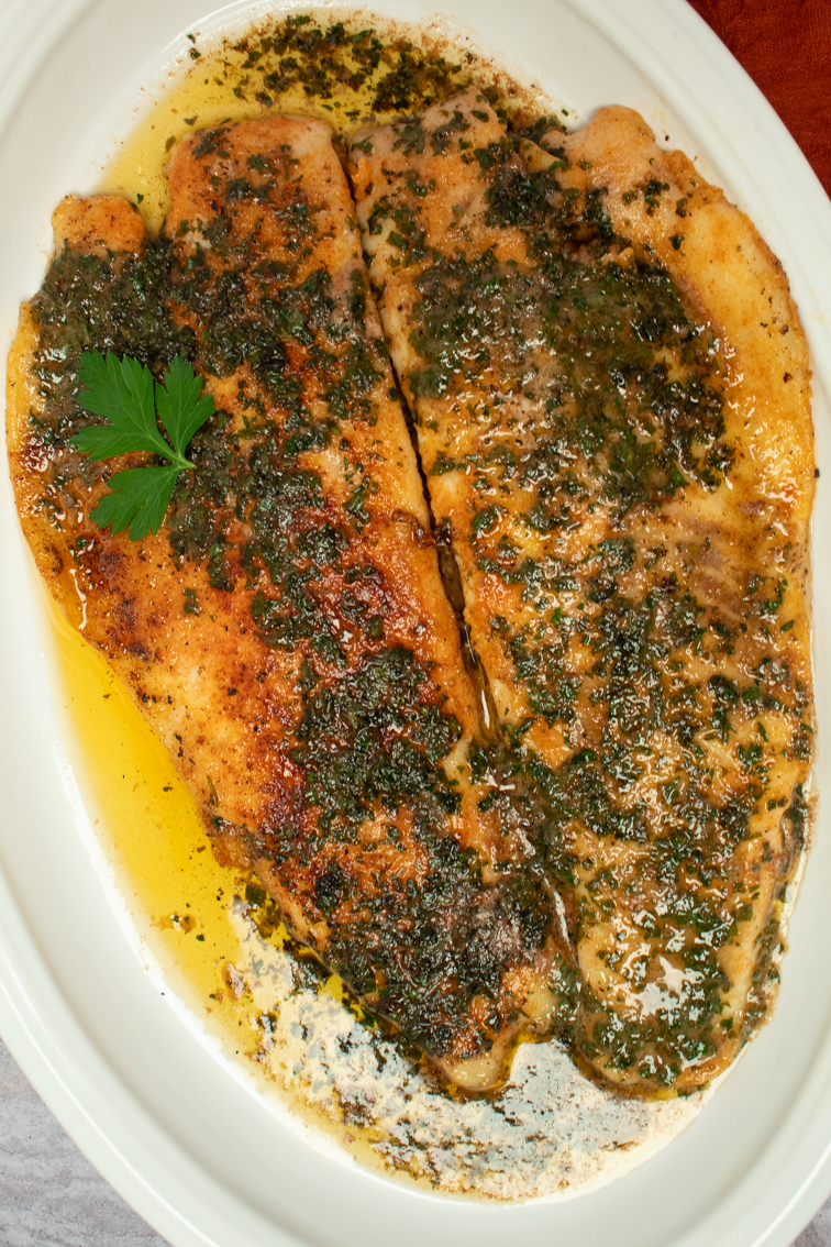 A closeup of two trout meunière fillets on a white serving platter.