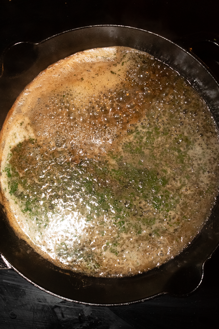 Trout meunière sauce in a black cast iron skillet.