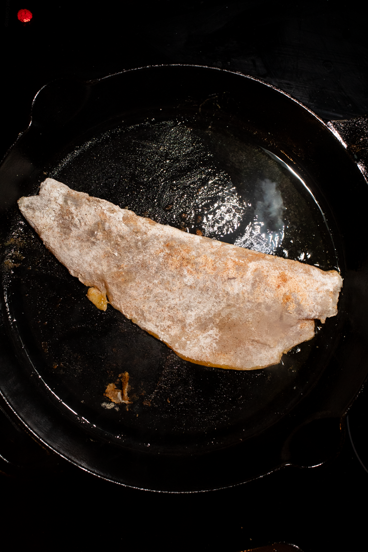 A trout fillet cooking in a cast iron pan.