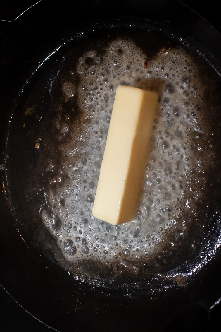 A stick of butter melting into browned butter in a cast iron skillet.
