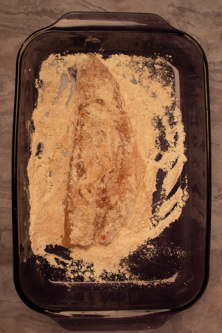 One trout fillet pressed into flour on the bottom of a glass baking dish.