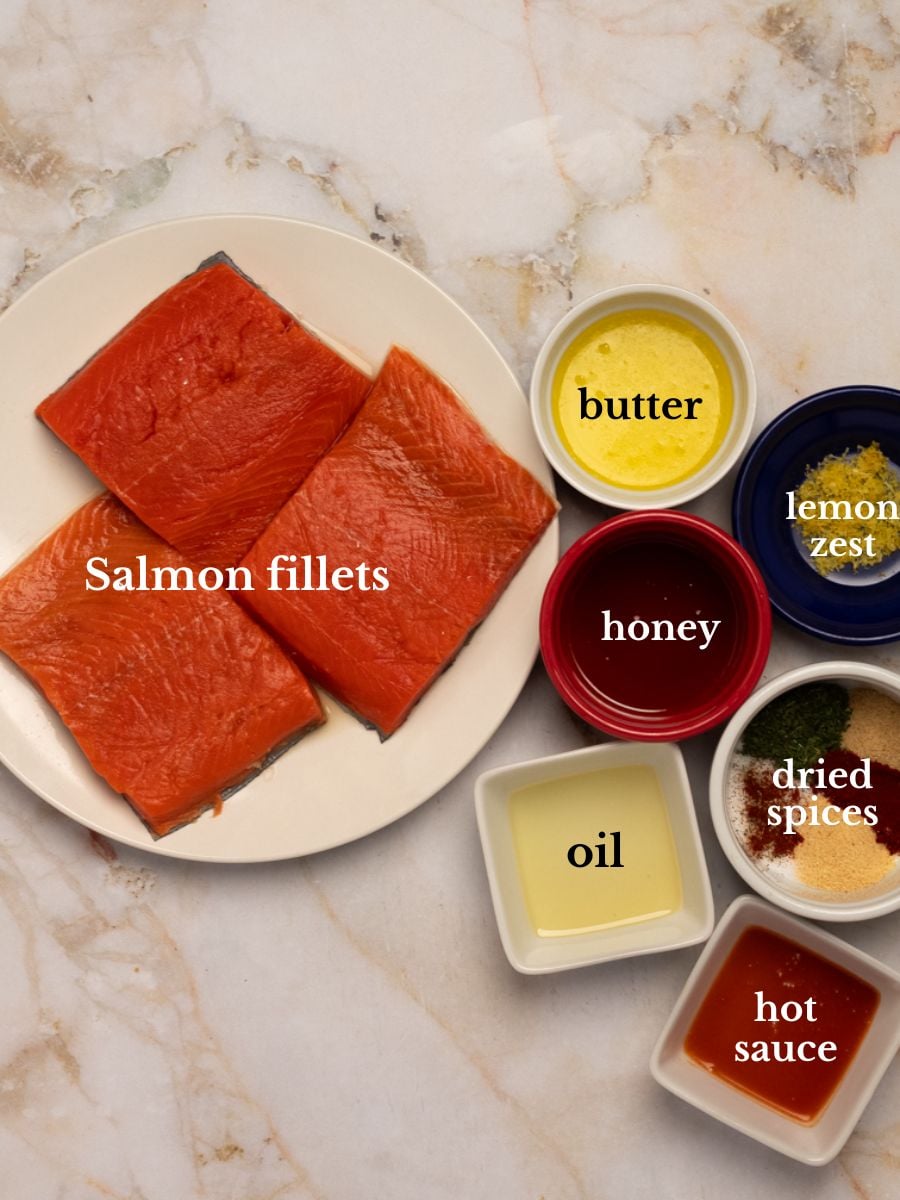 Ingredients for Cajun baked salmon on a plate an in bowls on a white marbled background.