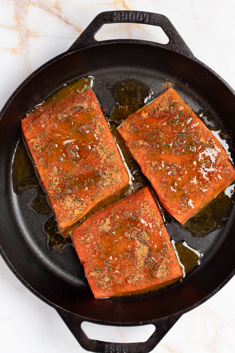 Honey butter sauce over Cajun-spiced salmon fillets in a black cast iron skillet.