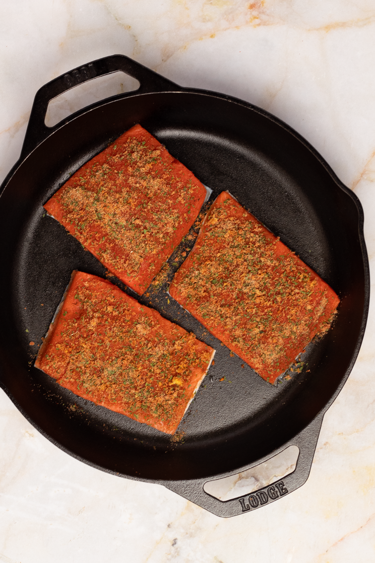 Seasoned salmon fillets in a black pan.