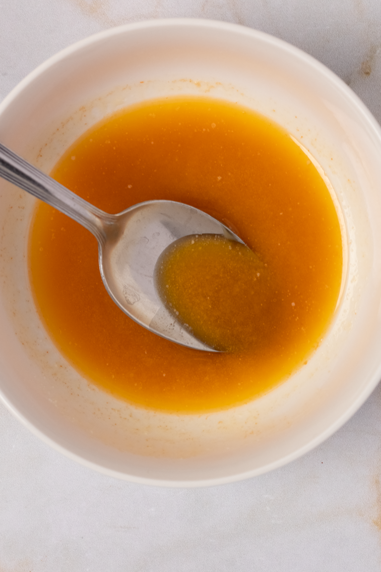 A buttery hot sauce with a spoon in a small round white bowl.