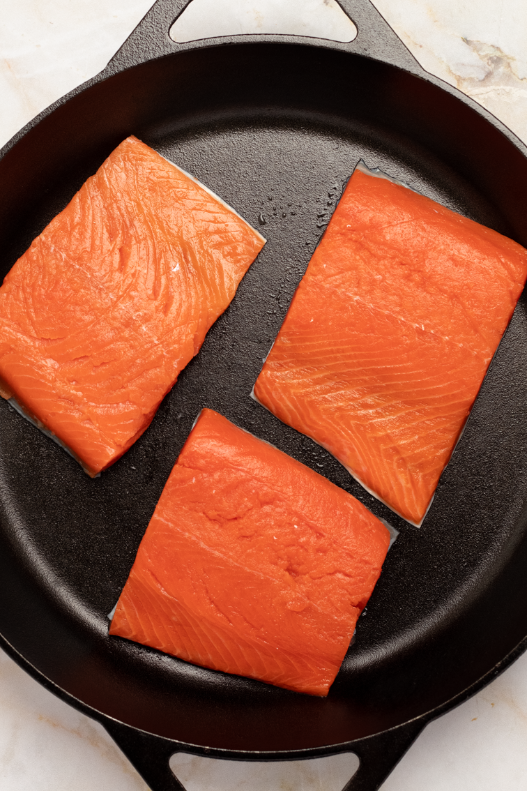 Three fresh sockeye salmon fillets in a lightly greased 12-inch cast iron skillet.