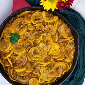 Cajun smothered yellow squash in a red enameled cast iron skillet with a green napkin and yellow and red flowers.