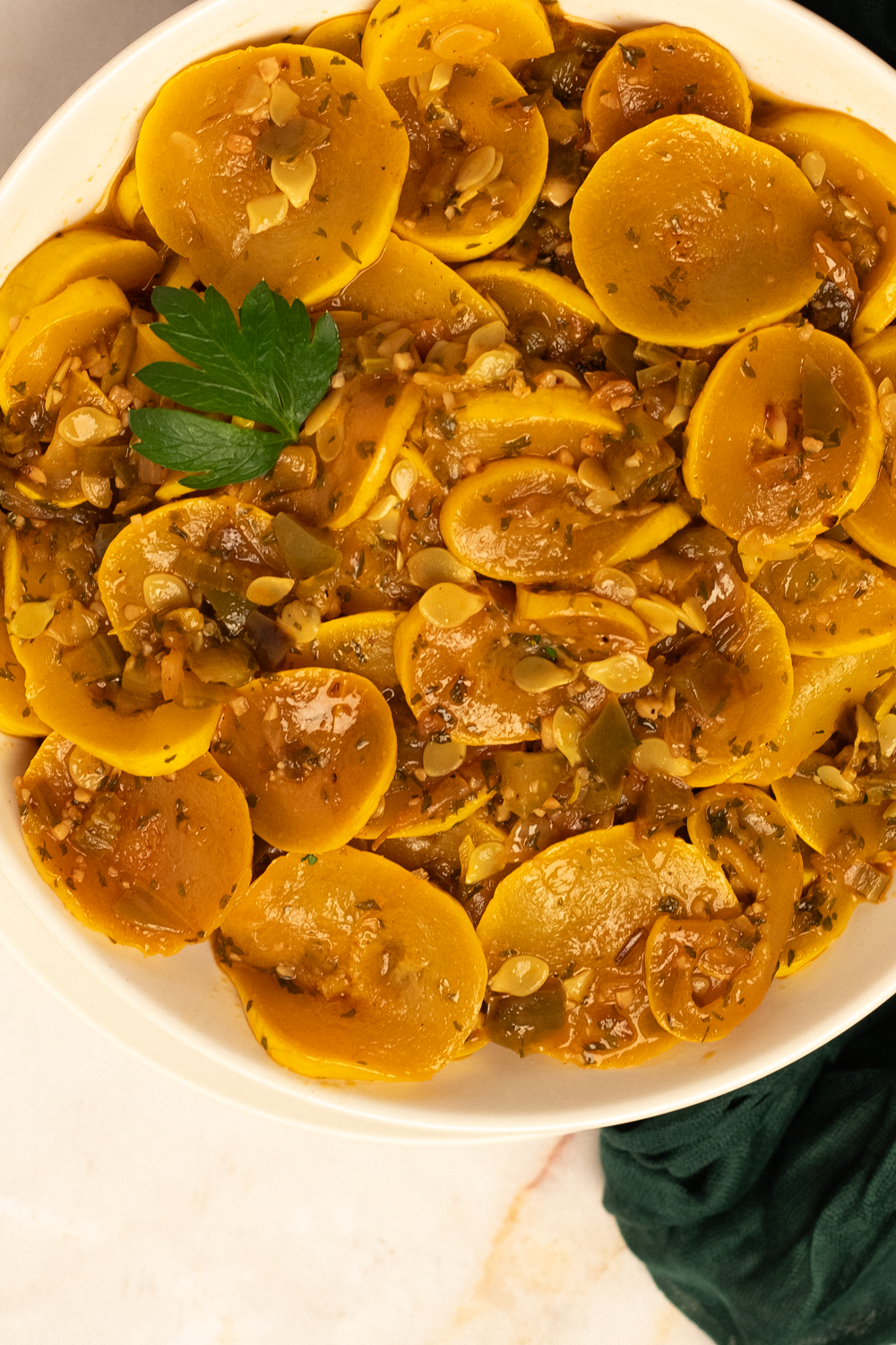 A round white bowl filled with Cajun smothered yellow squash with a whole parsley leaf garnish in the top left corner. 