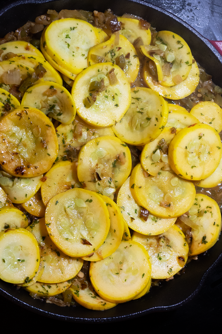Cajun smothered yellow squash cooking in an enameled cast iron skillet.
