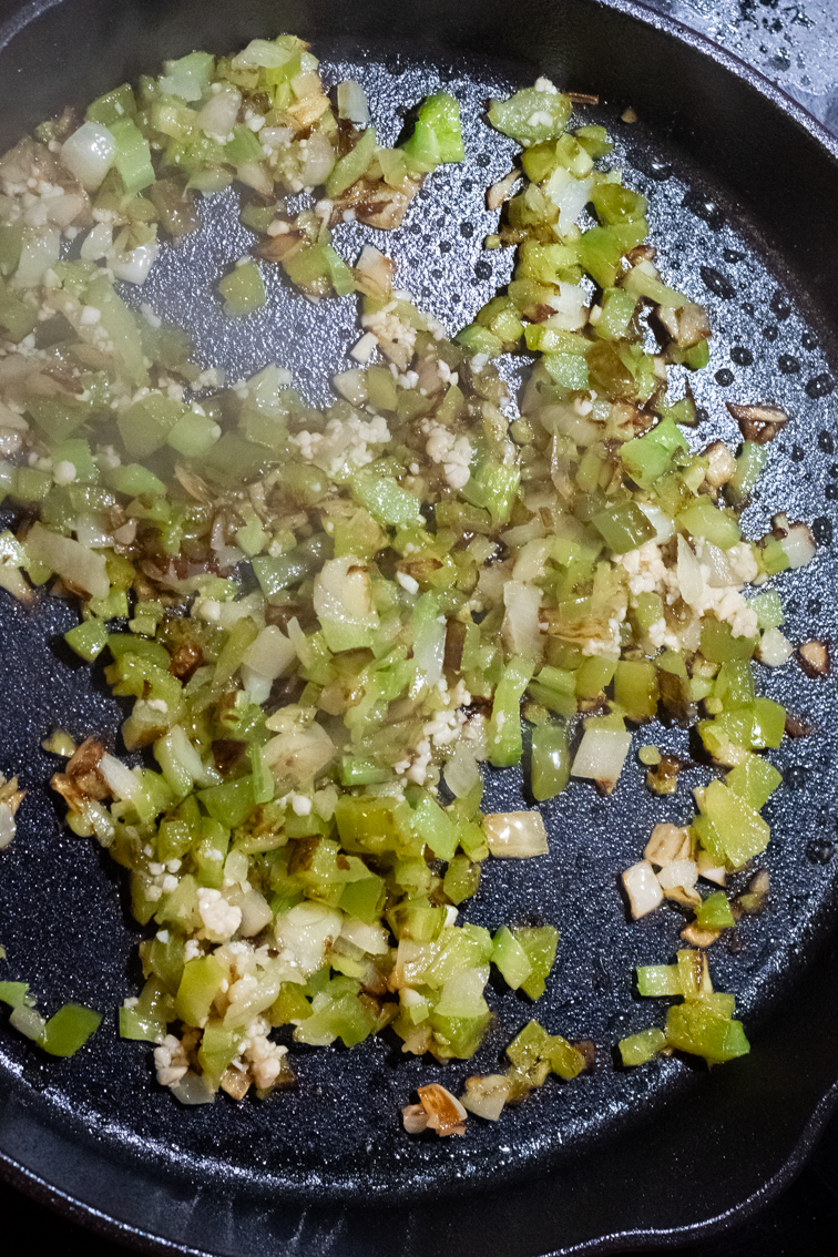 Browned garlic and chopped Cajun trinity vegetables in a black skillet.