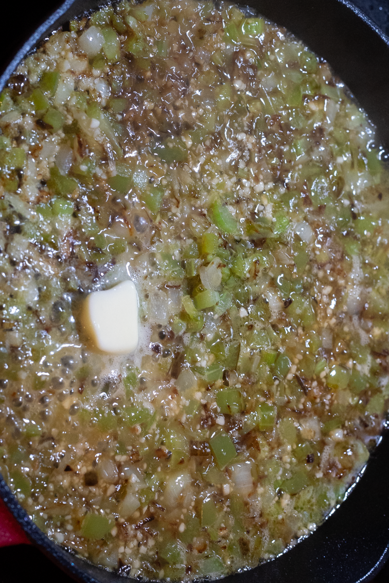 Chicken broth and browned vegetables and garlic in a pan on the stove.