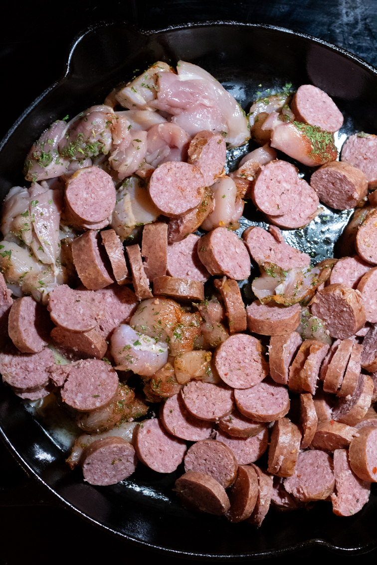 Raw sausage and chicken in a skillet.