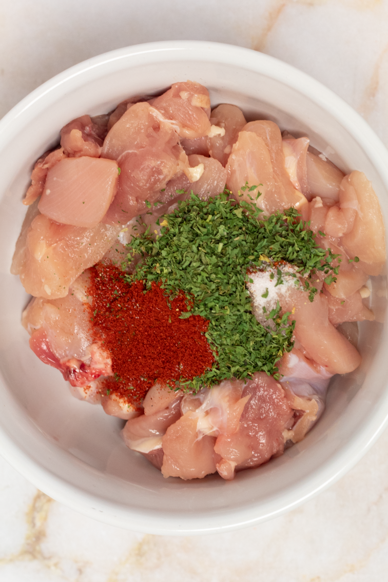 Chopped chicken thigh pieces topped with dried spices in a white bowl.
