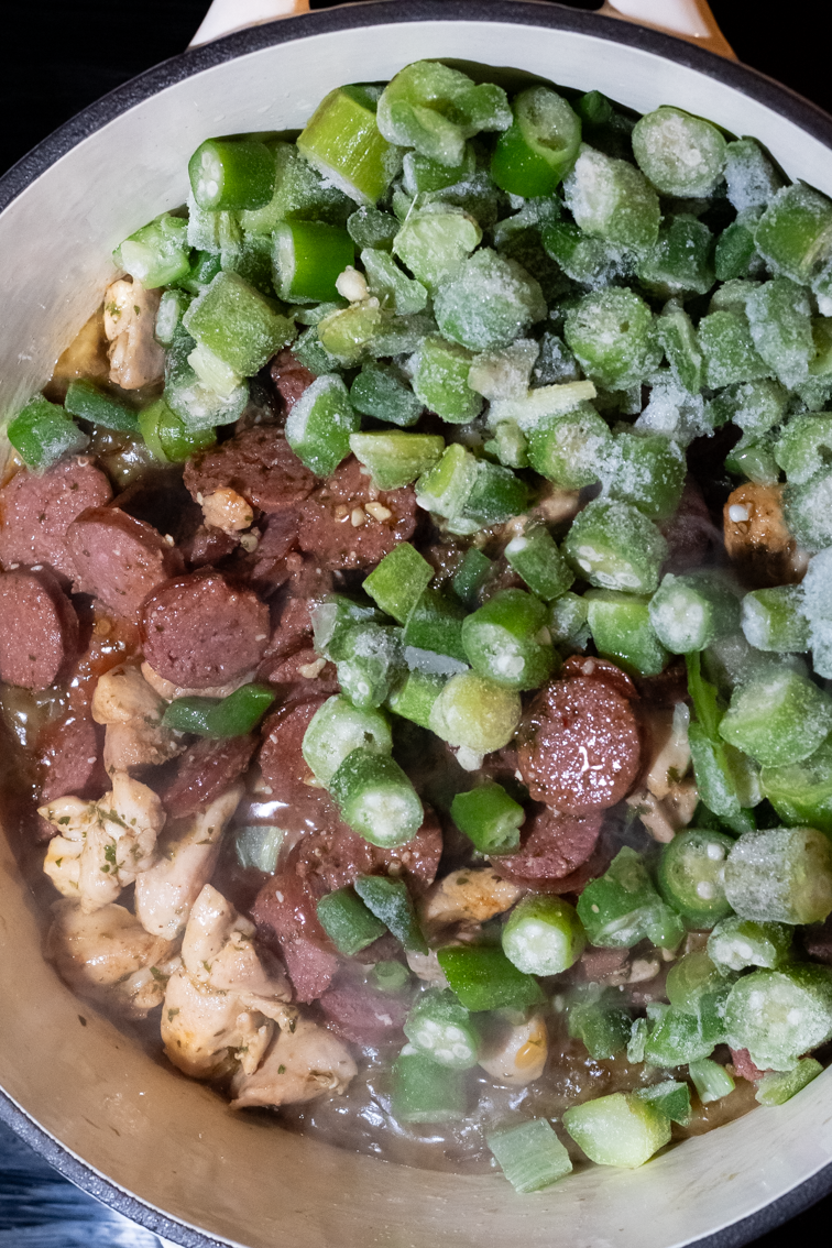 Roux, browned meats, and frozen okra in a pot.