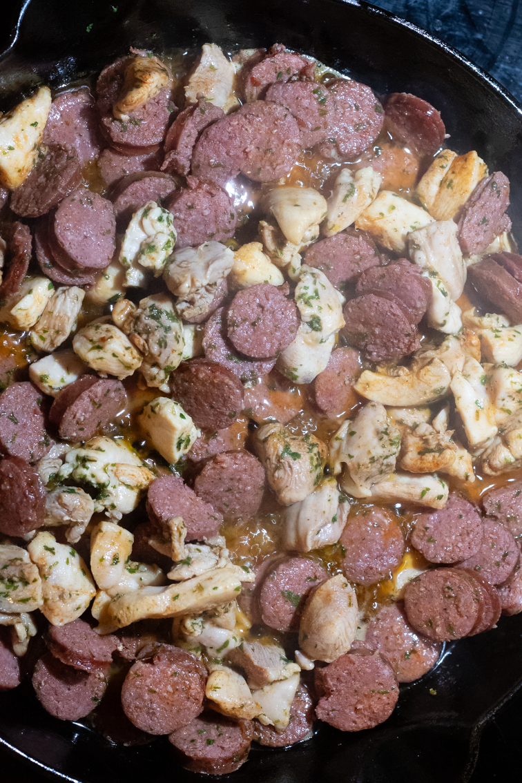 Browned, seasoned chicken thighs and sausage in a pan.