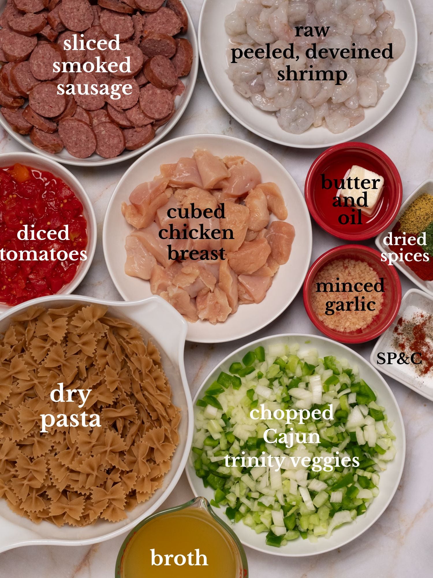 Labeled ingredients for pastalaya in bowls on a white marble background.