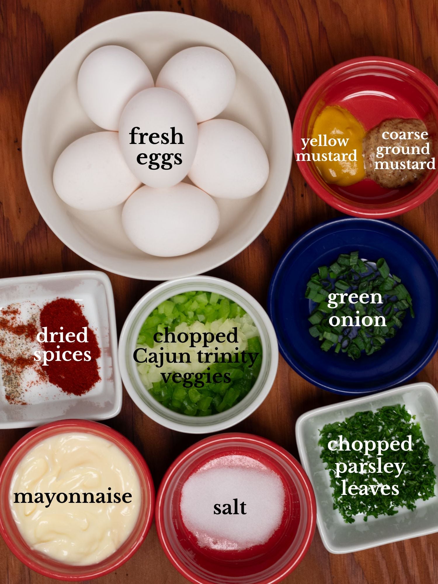 Ingredients for Cajun deviled eggs in bowls on a brown wooden background.