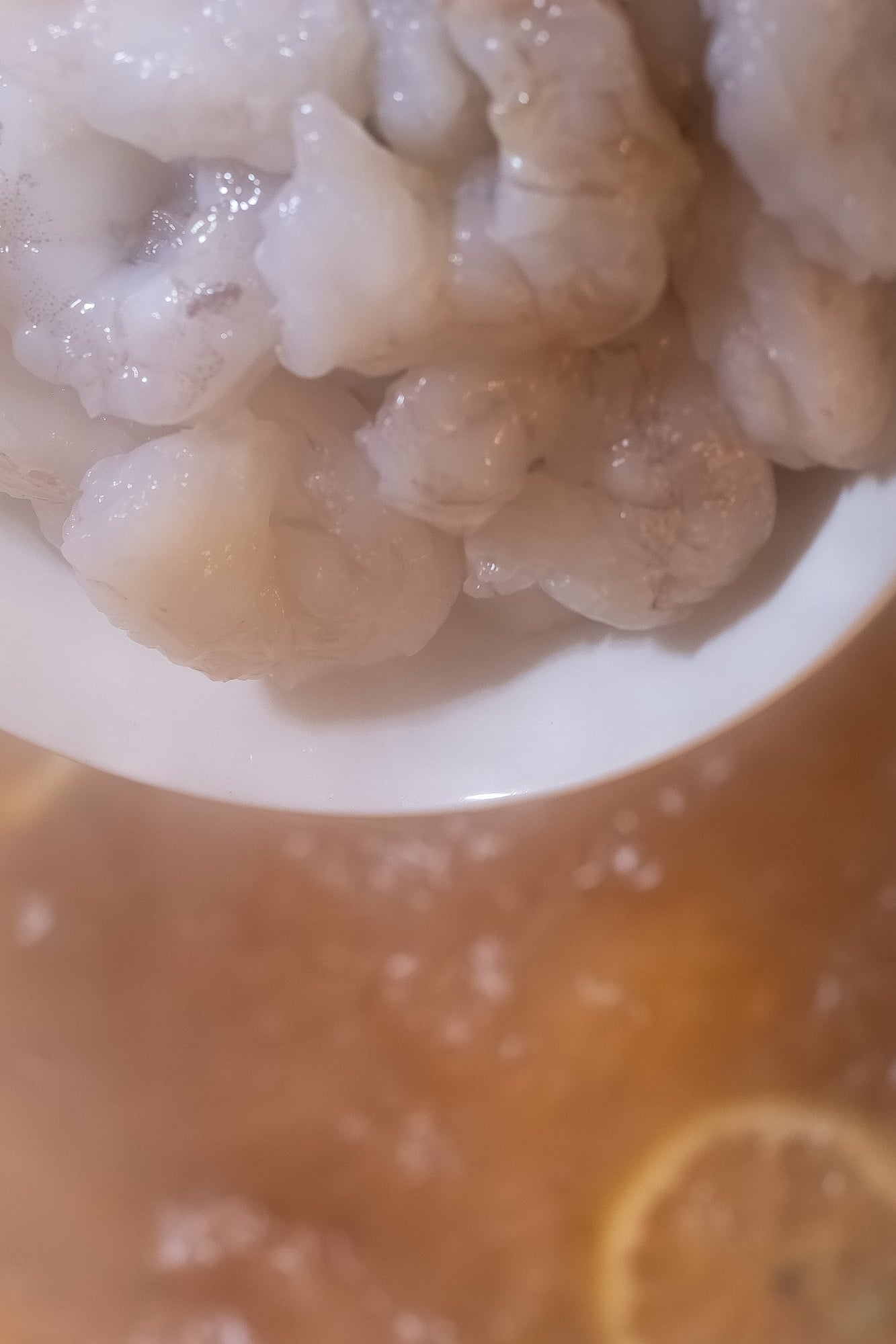 A bowl of raw, peeled and deveined shrimp over a pot of boiling poaching liquid.