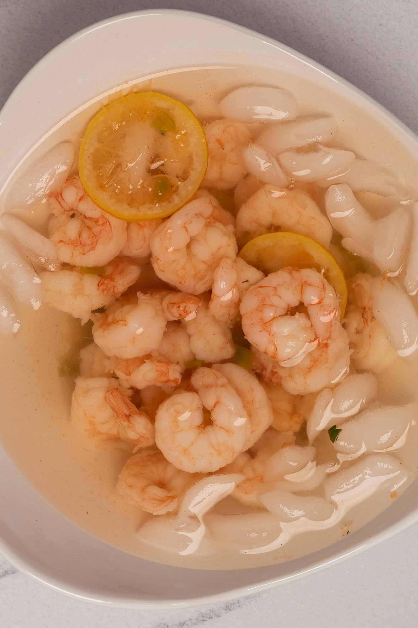 Poached shrimp submerged in an ice water bath in a white serving dish.
