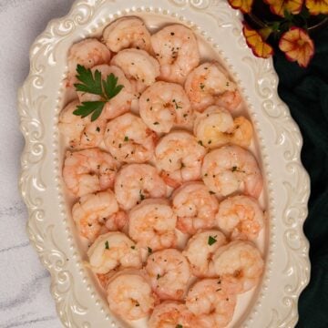 Square image of poached shrimp on an oval antique-look serving platter.